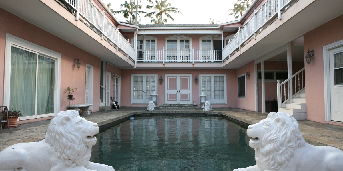Pink estate house courtyard with a pool guarded by two white stone lion statues